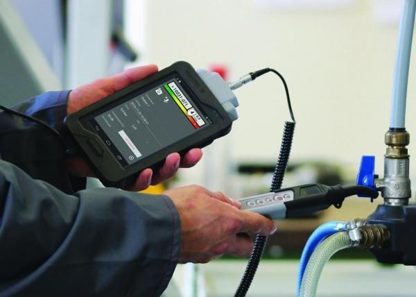 Person using a handheld device connected to a pipe, likely measuring something; in a workshop.