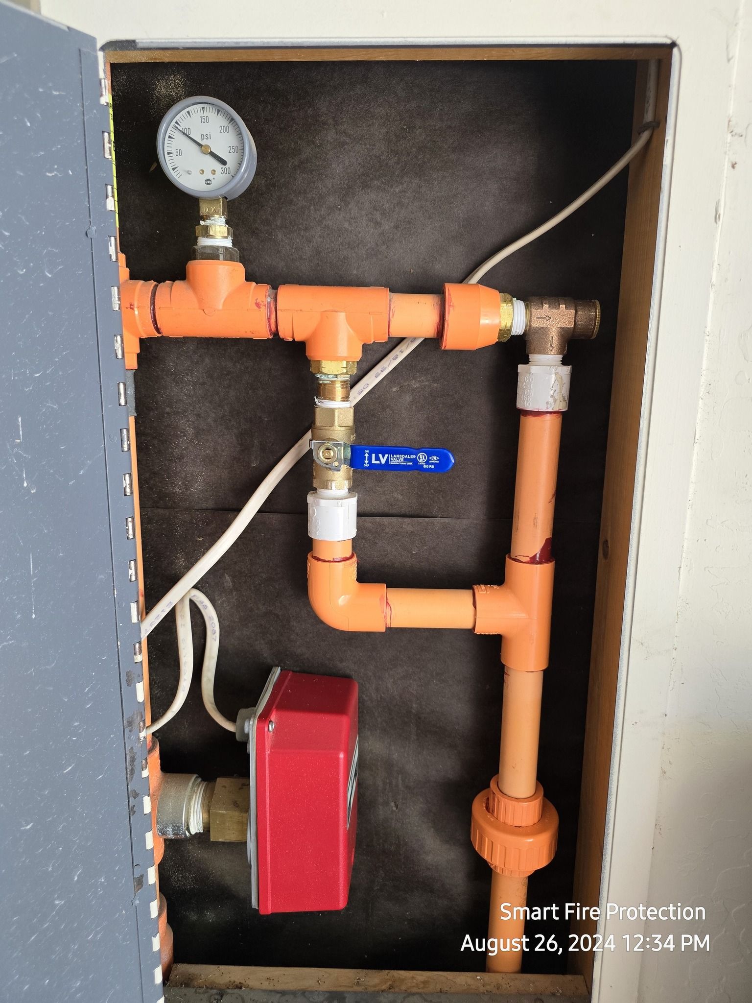Orange PVC pipes with a pressure gauge and valve, likely part of a water system, installed in a wall.