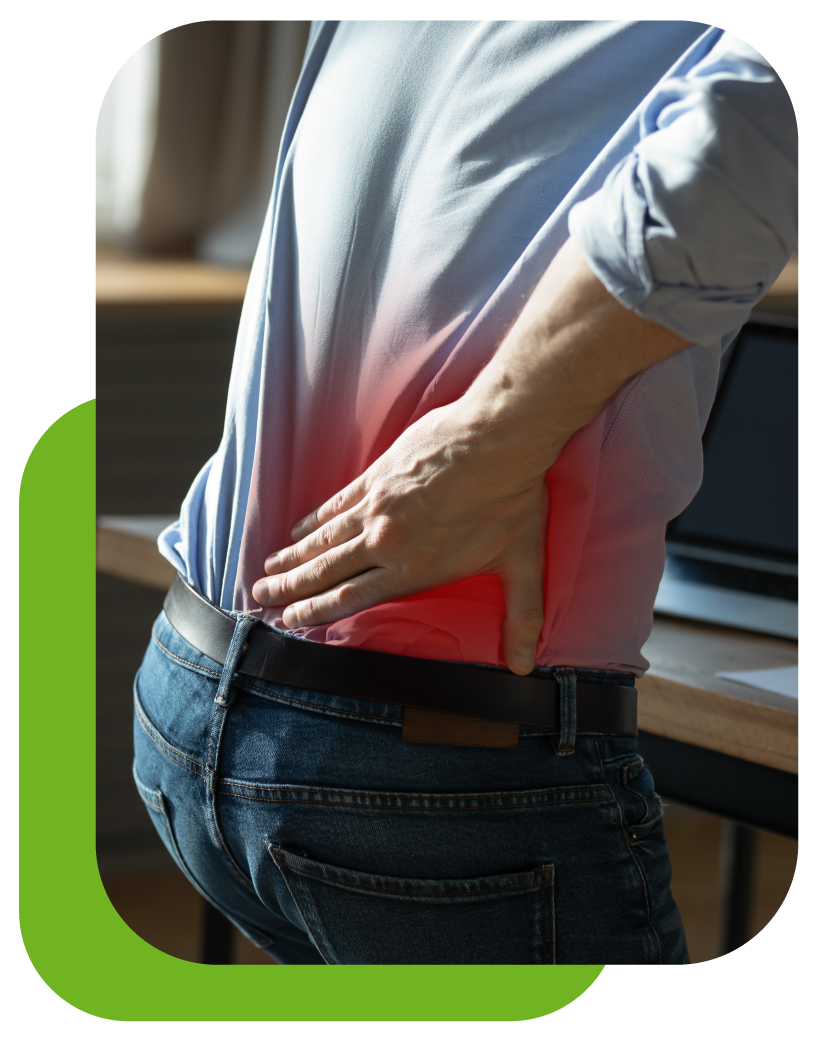 A man is holding his back in pain while sitting at a desk.