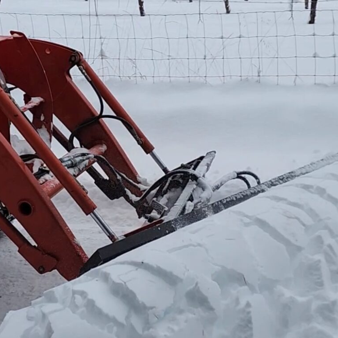 A red tractor is sitting in the snow near a fence