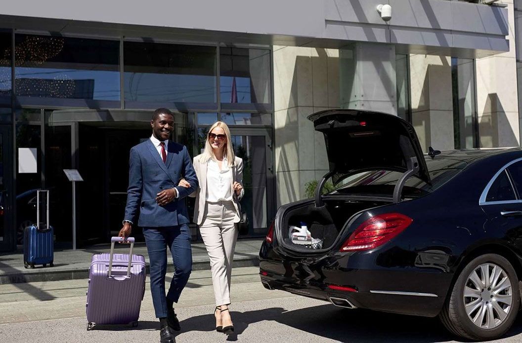 A man and a woman are walking towards a car with their luggage.