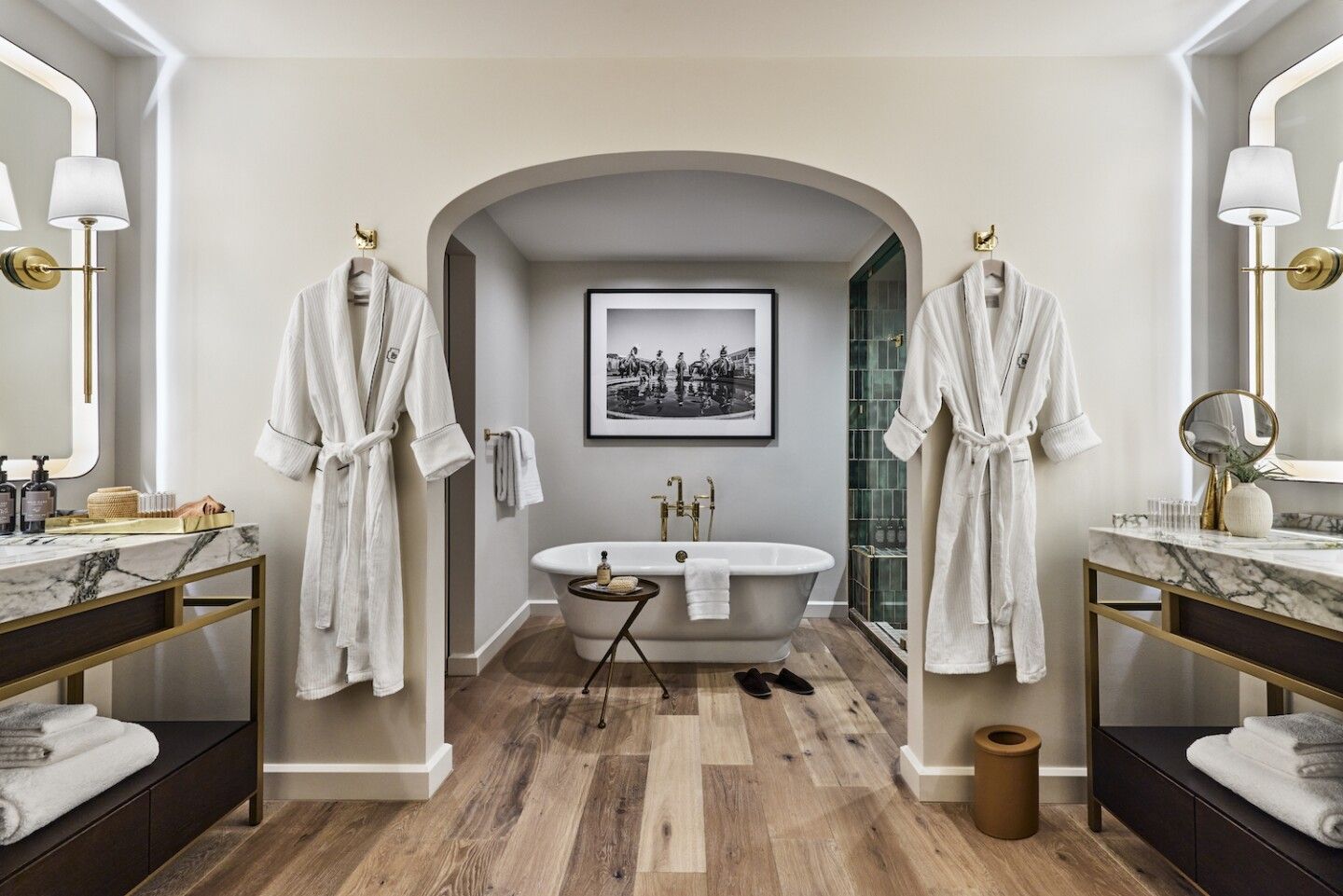 A bathroom with two sinks , a bathtub and two robes hanging on the wall.