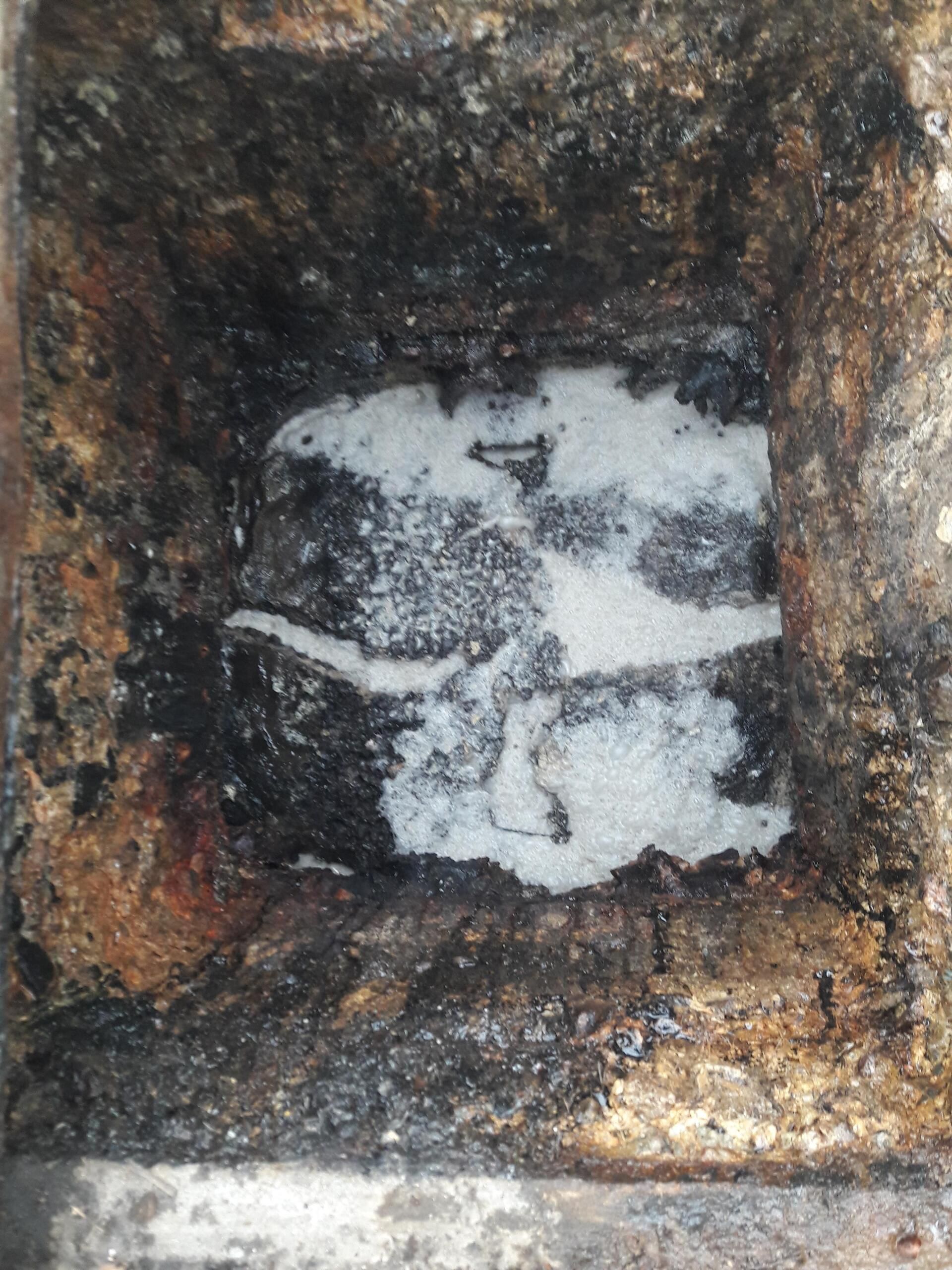 Square metal drain with white, powdery substance and dark debris.