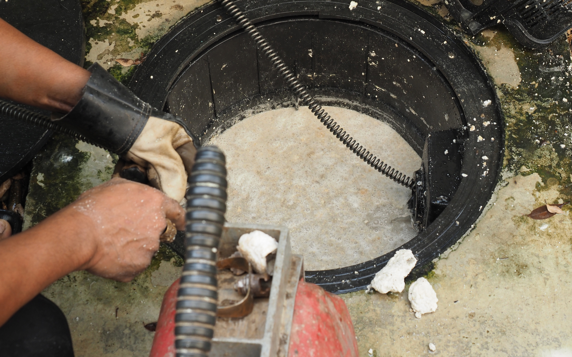 Worker using a tool to clear grease trap.