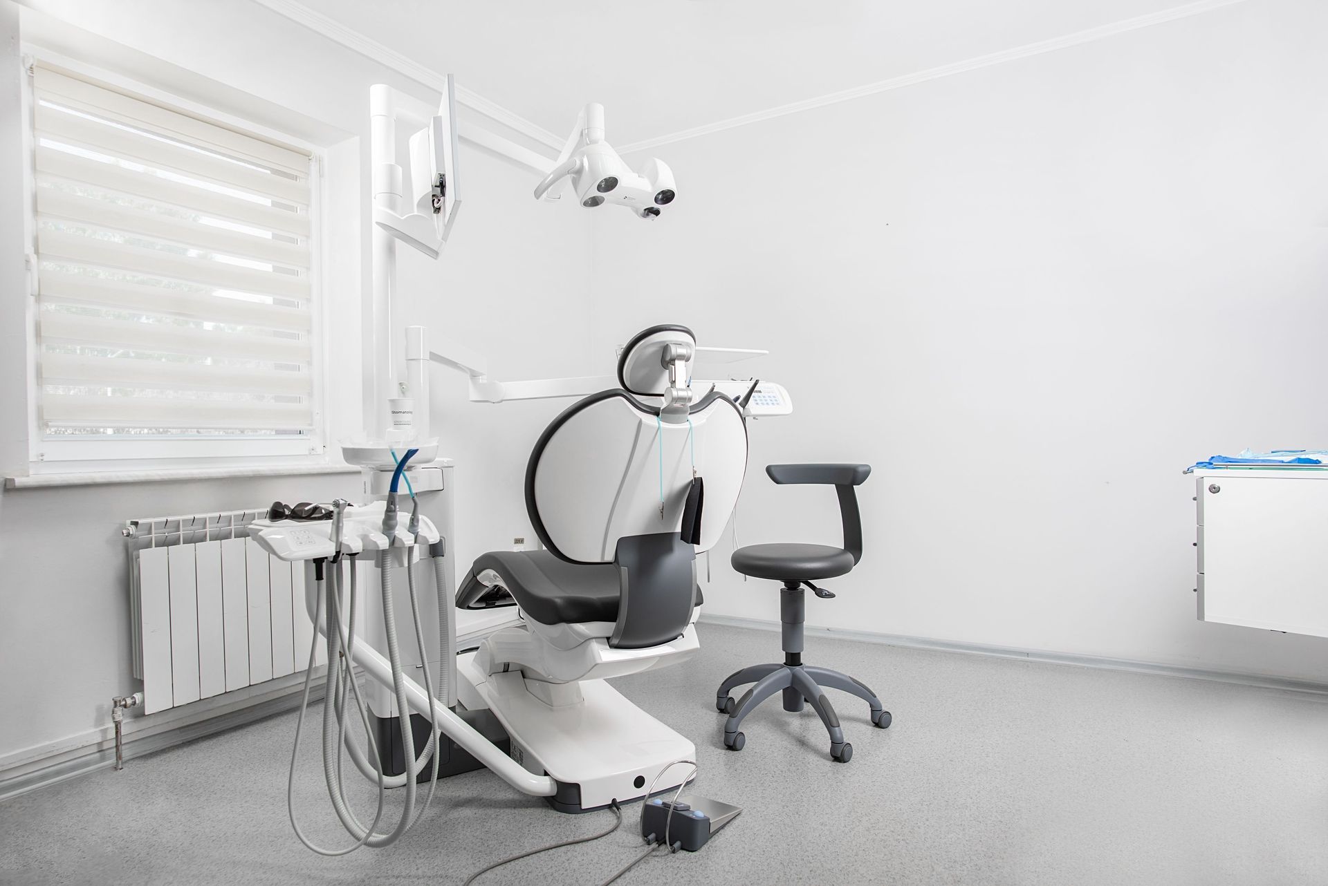 Empty dental exam room with chair, overhead light, and tools by a window