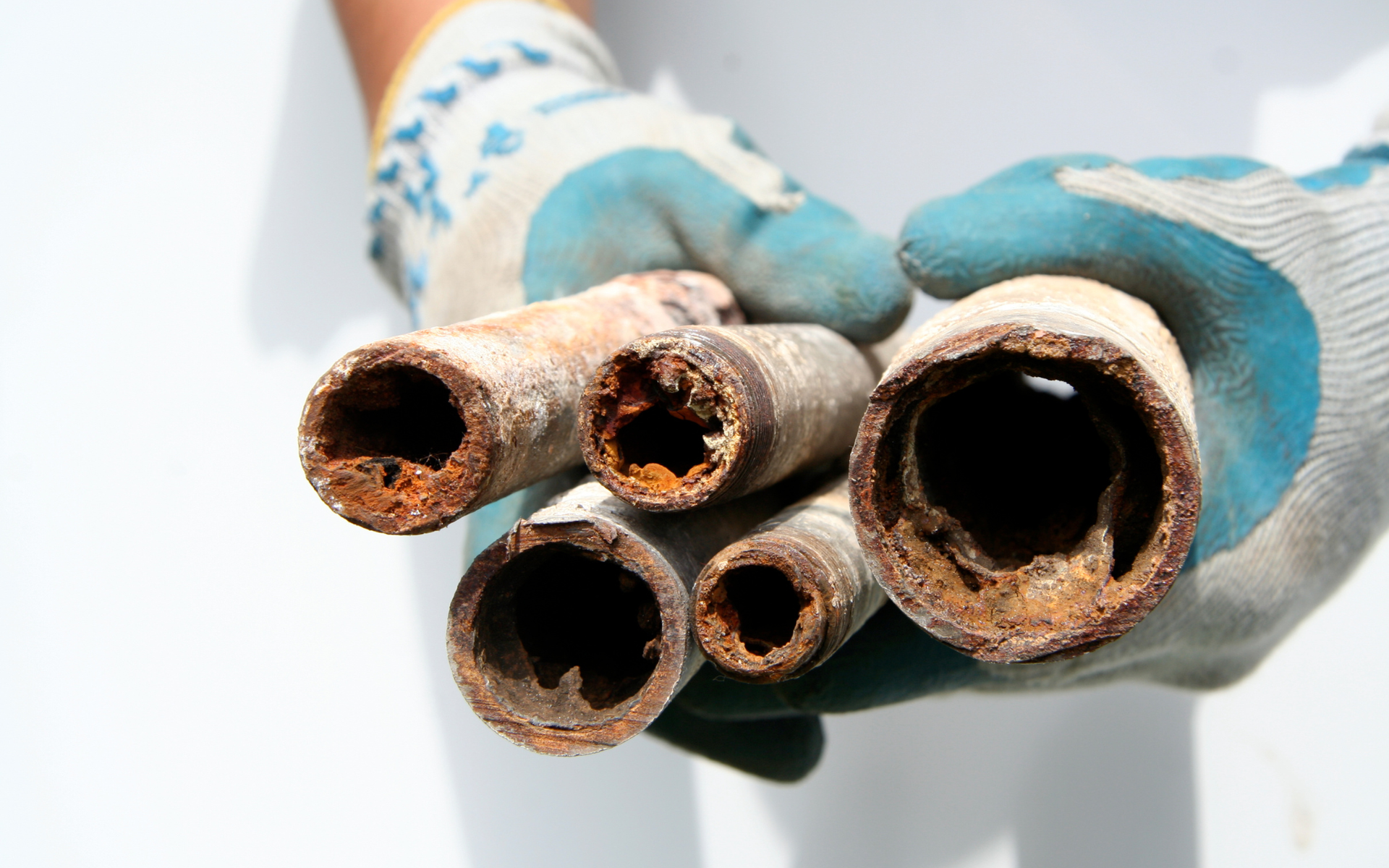 Rusty metal pipes held in gloved hands, showing corroded openings close up.