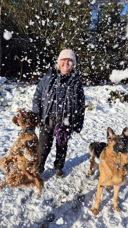 Woman and two dogs in snow, smiling, with snow falling.