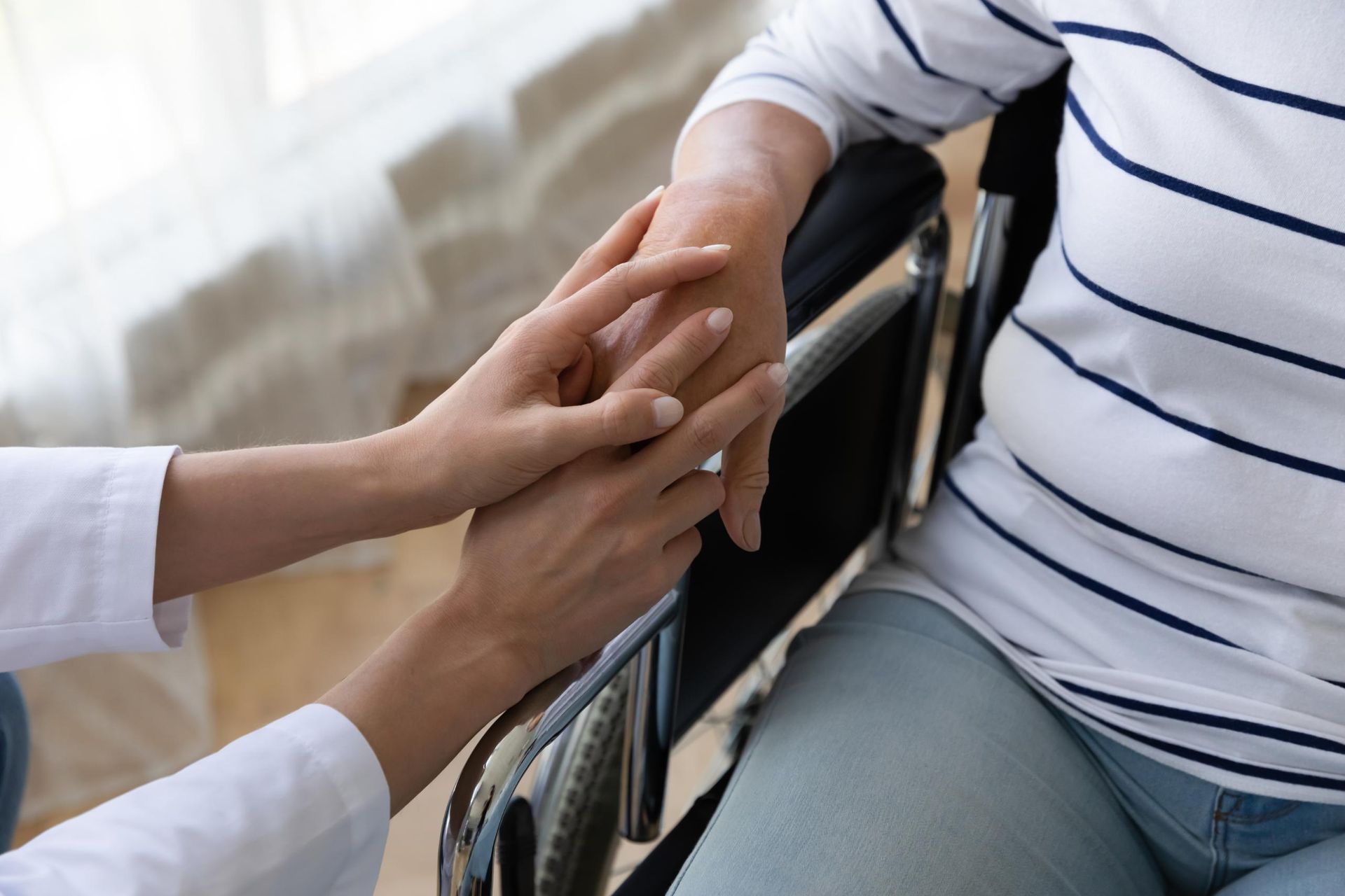 A person in a wheelchair has their hand held by someone wearing a white coat.
