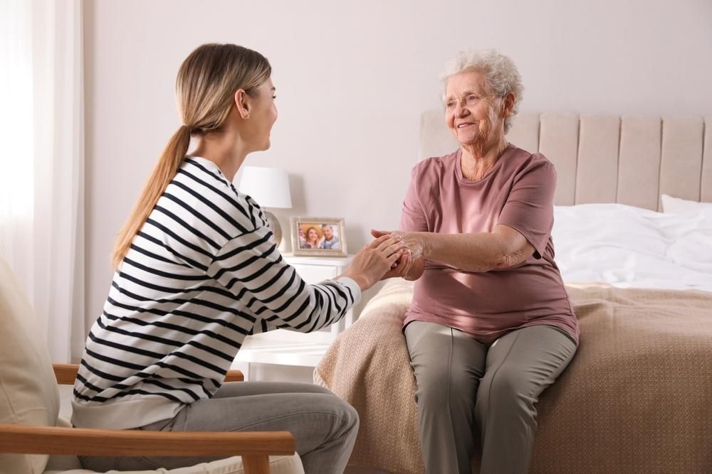 Woman in striped shirt holds hands with smiling person on bed. Interior bedroom.