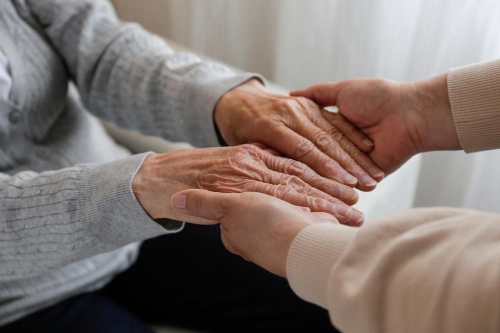 Two pairs of hands clasped together, providing comfort and support.