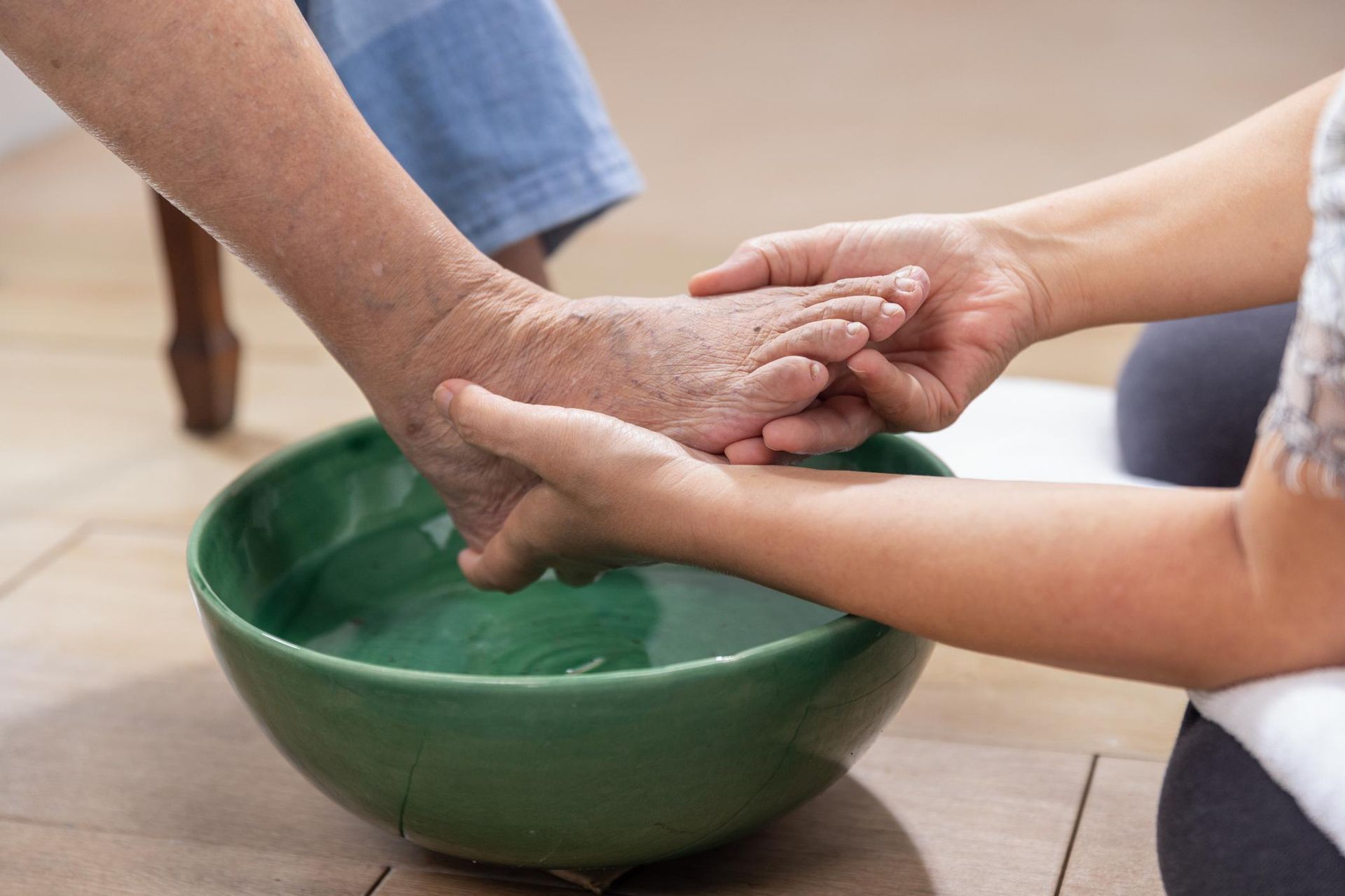 Person washing another person's foot in a green bowl of water.