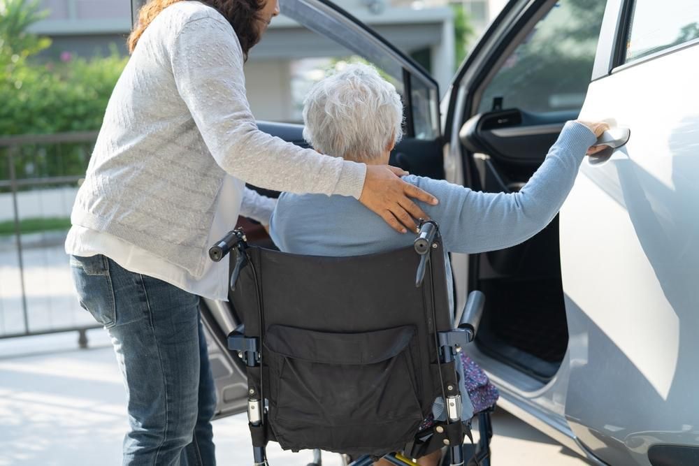 Woman helping another out of wheelchair and into car.