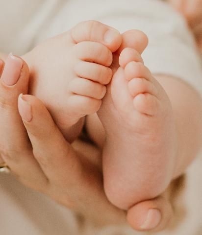 Close-up of a baby's tiny feet being held in a person's hands. Skin tones are fair.