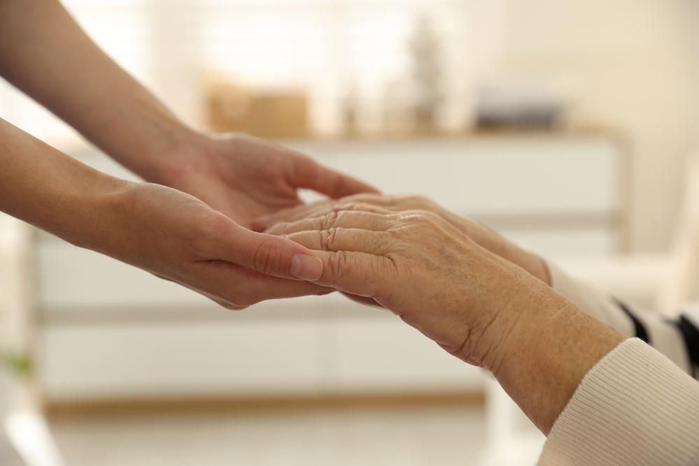 Younger hand holding the hand of an older person, offering comfort indoors.