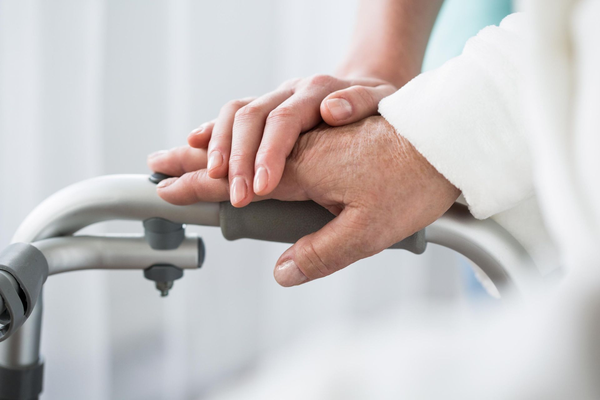 Hands of person and caregiver on a walker.