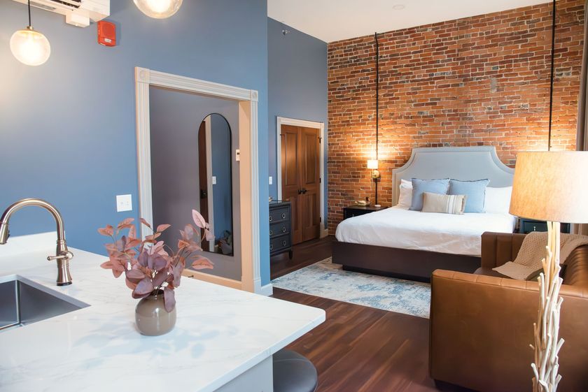 Hotel suite with a brick wall, bed, kitchenette, and seating area.
