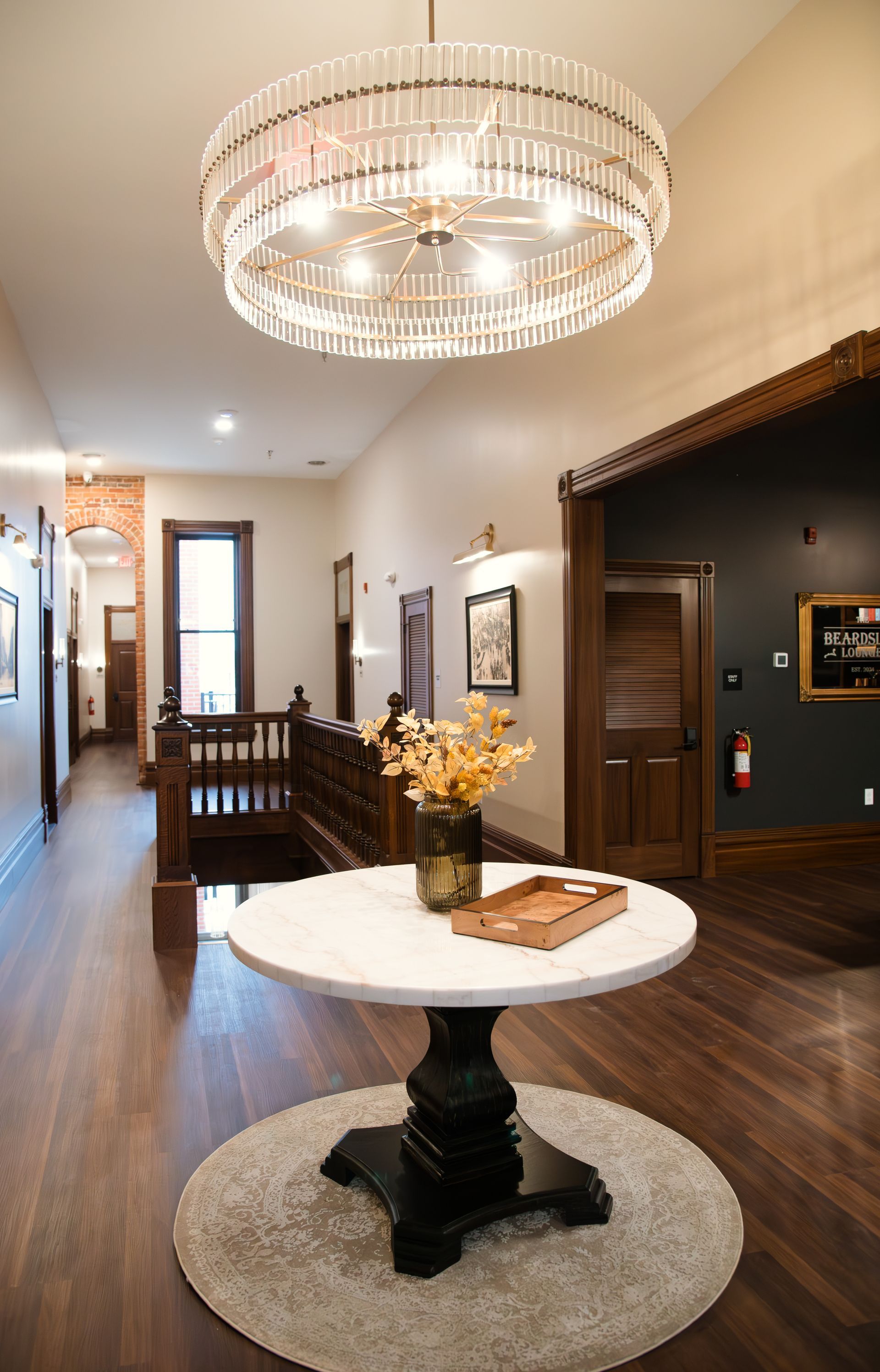 Hallway with a round marble-top table and large chandelier. Dark wood accents, hardwood floors.