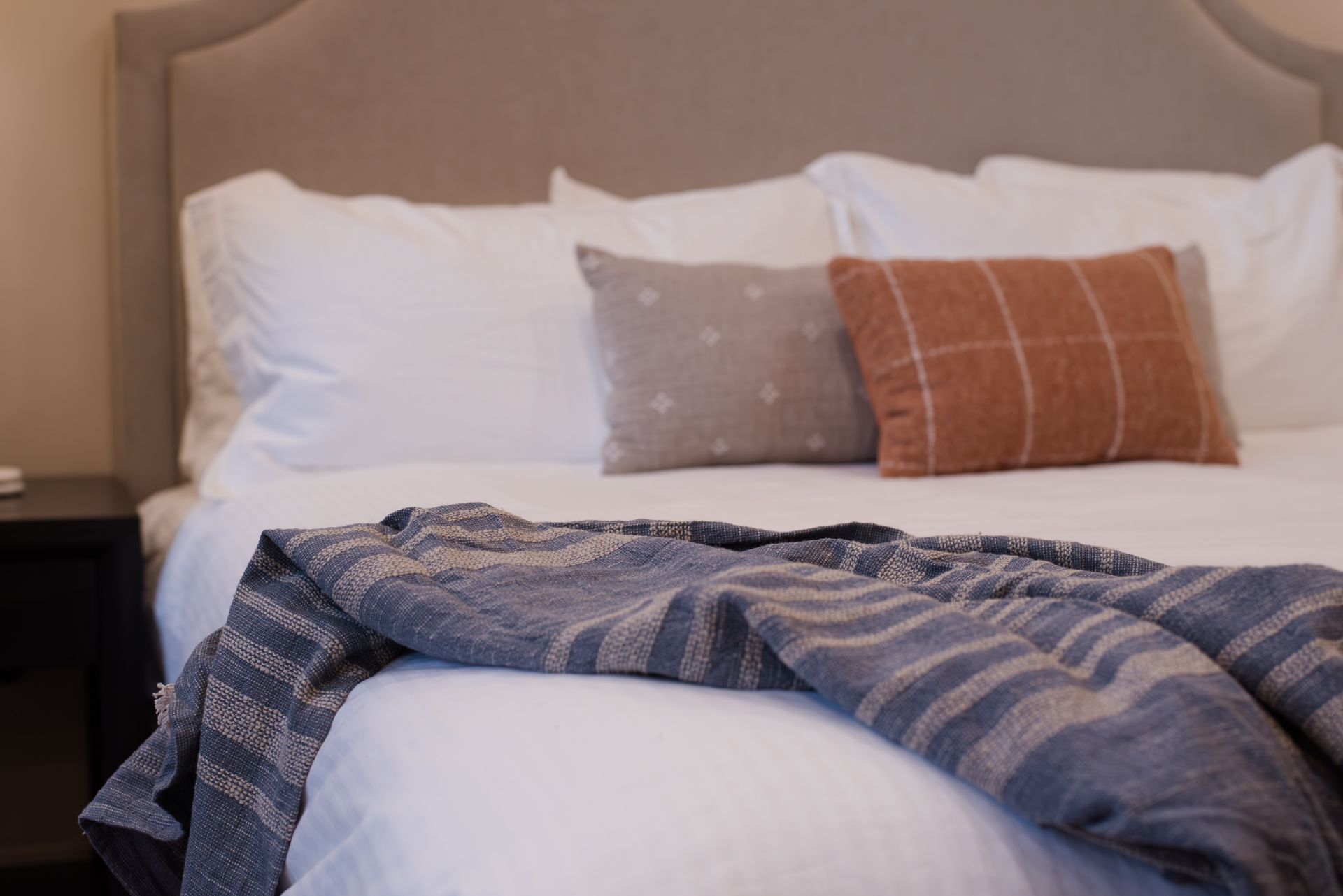 Bed with white linens, decorative pillows in beige and orange, and a blue throw blanket.