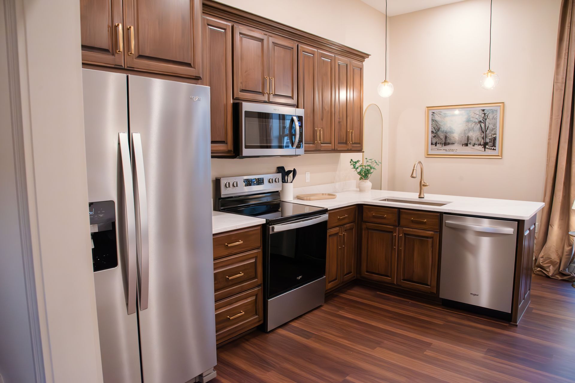 A compact kitchen with dark wood cabinets, stainless steel appliances, and white countertops.