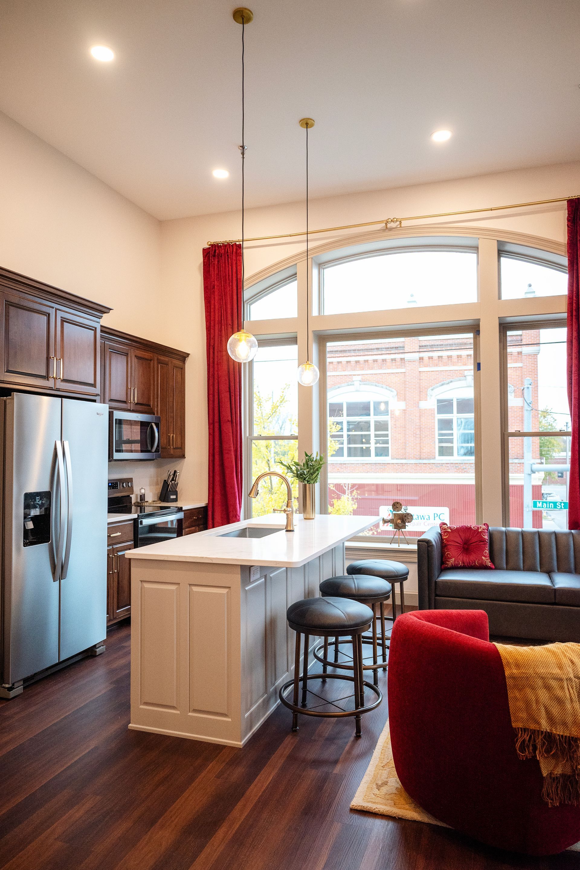 Modern kitchen with island, bar stools, red accents, and large arched window.