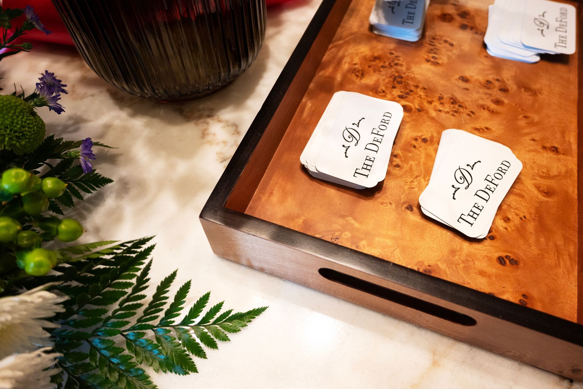 Tray with branded cards, flowers, and a glass on a marble surface.