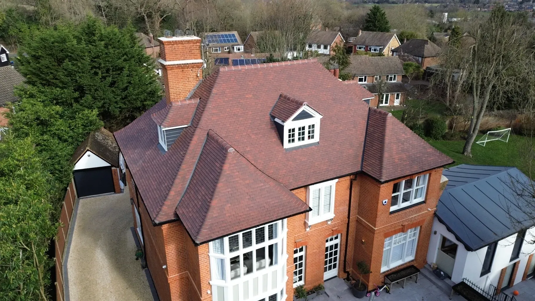 An aerial view of a large brick house with a red tile roof.