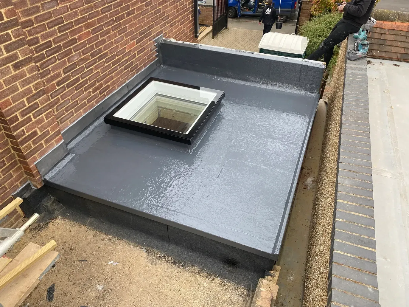 A man is standing on a roof with a skylight on it.