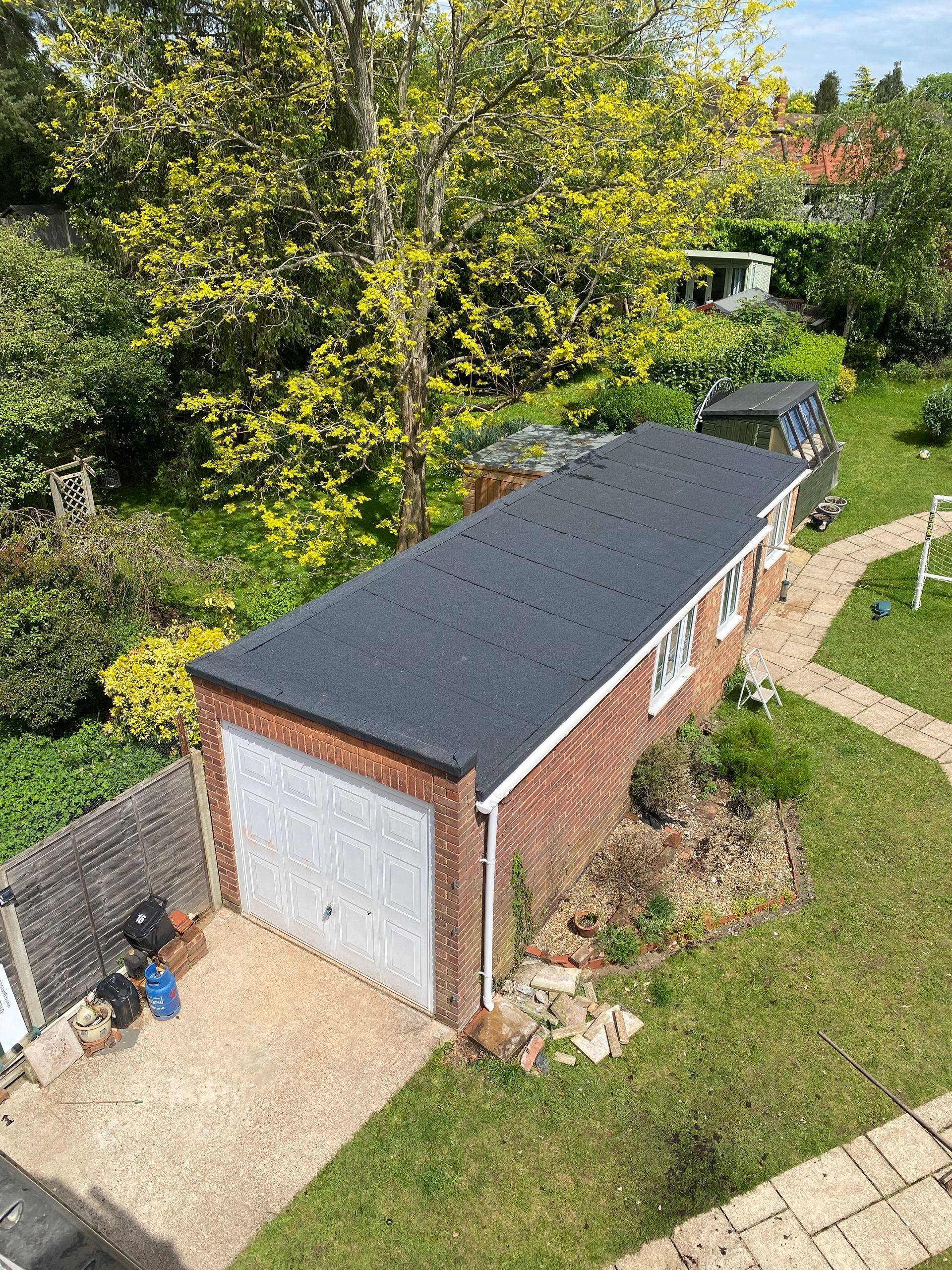 an aerial view of a garage with a flat felt roof in a garden .