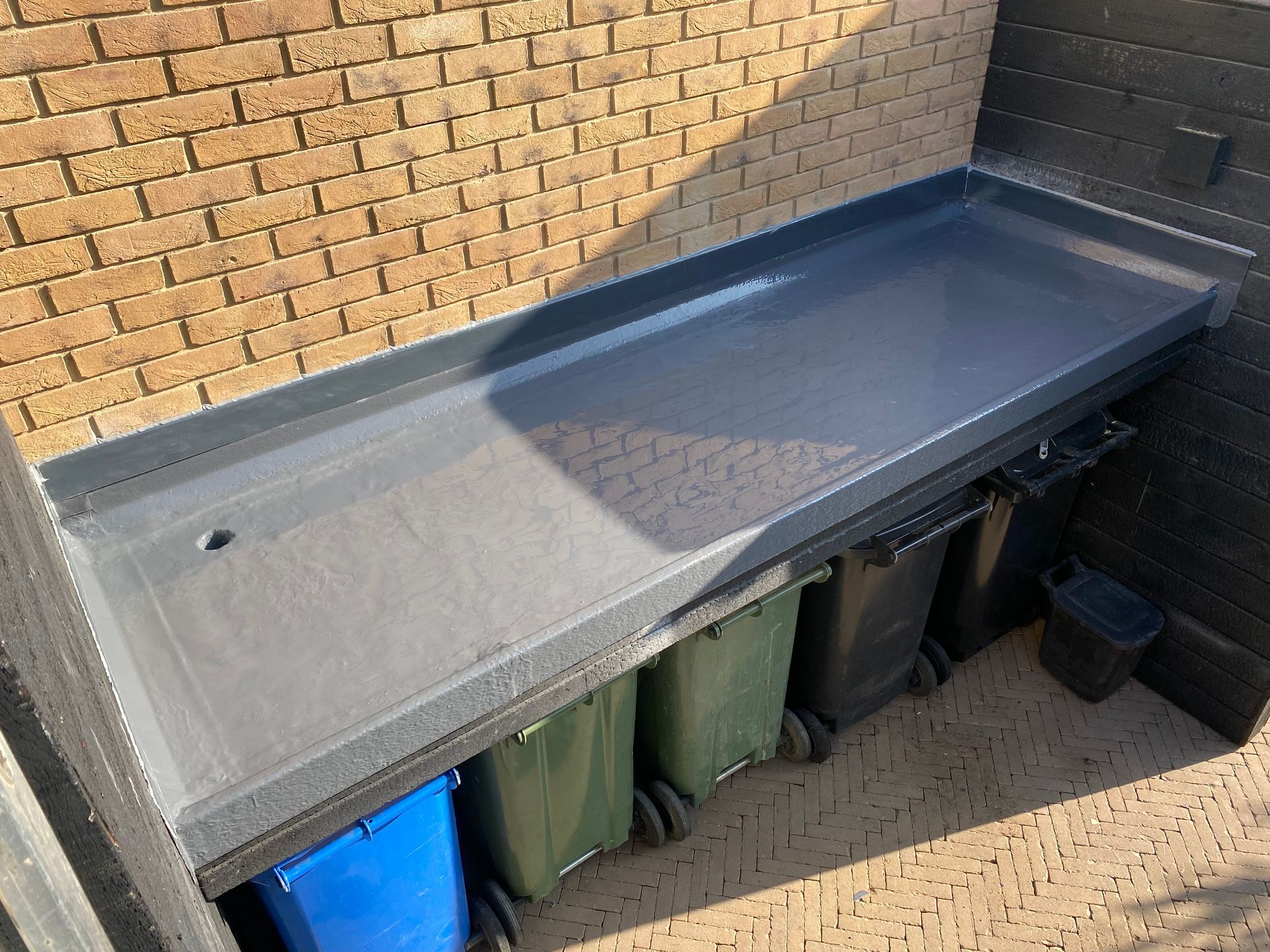 a brick wall with a table and wheelie bins underneath it .