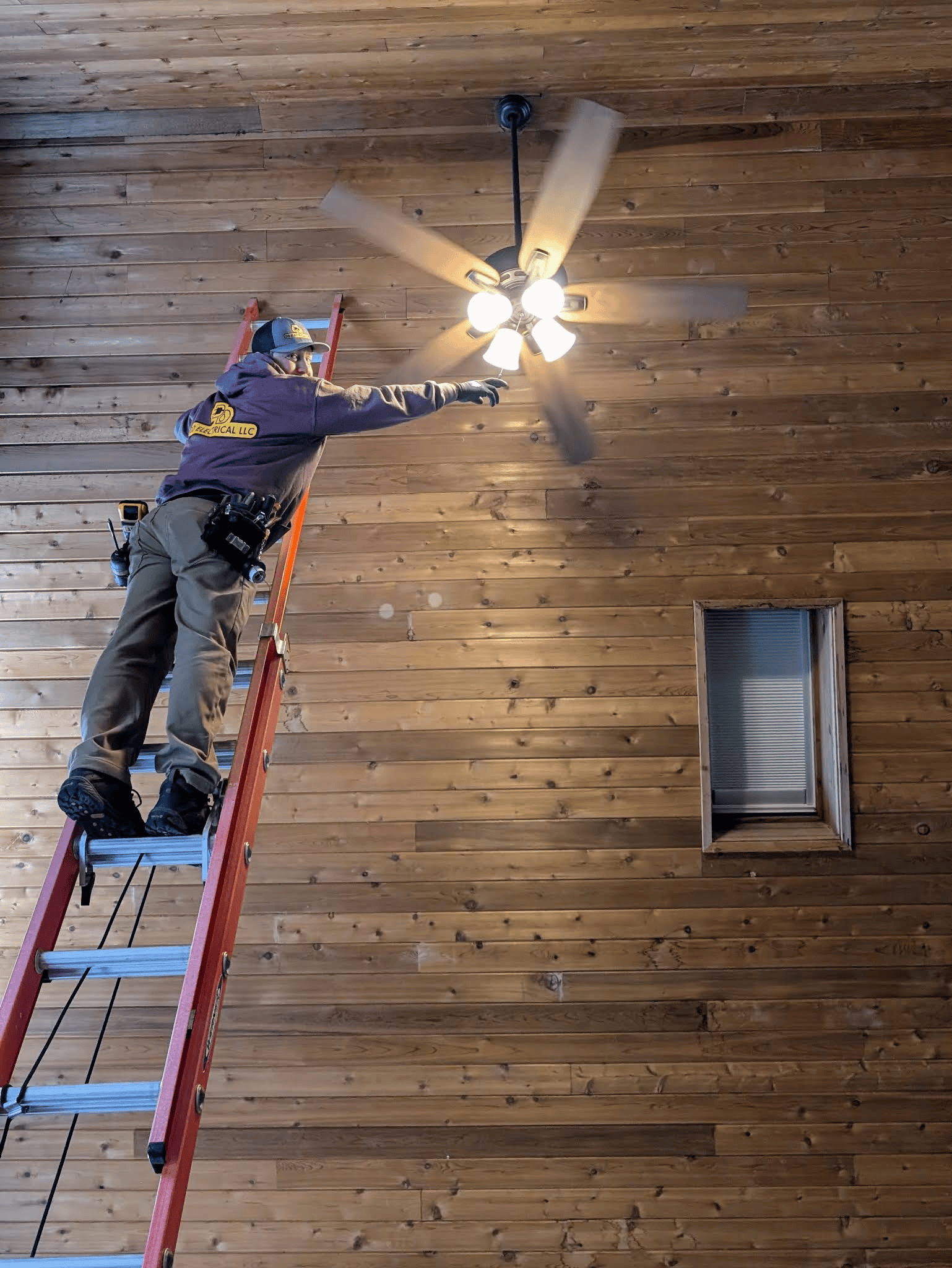 A man is standing on a ladder fixing a ceiling fan.