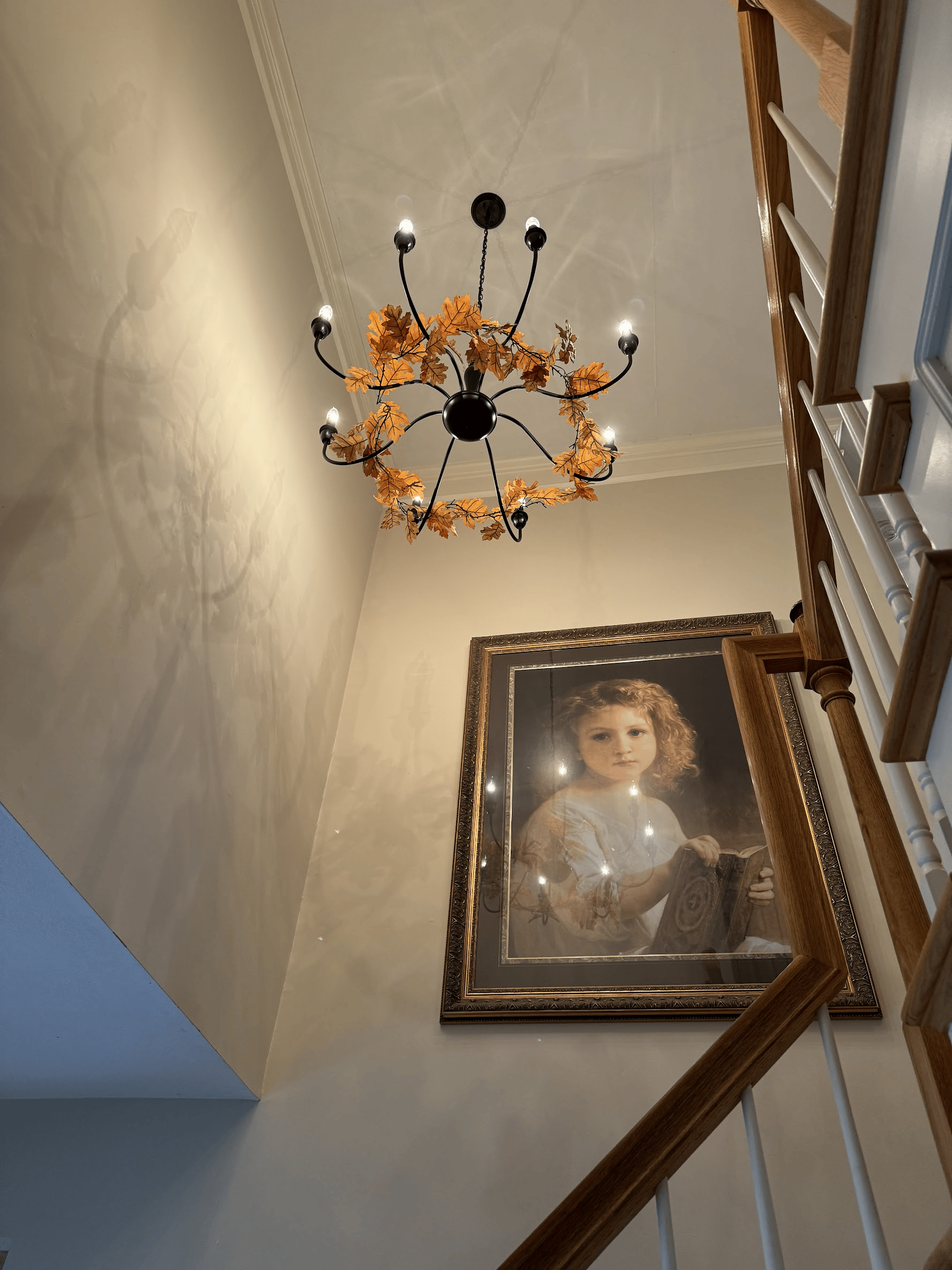 A staircase with a chandelier hanging from the ceiling and a painting on the wall.