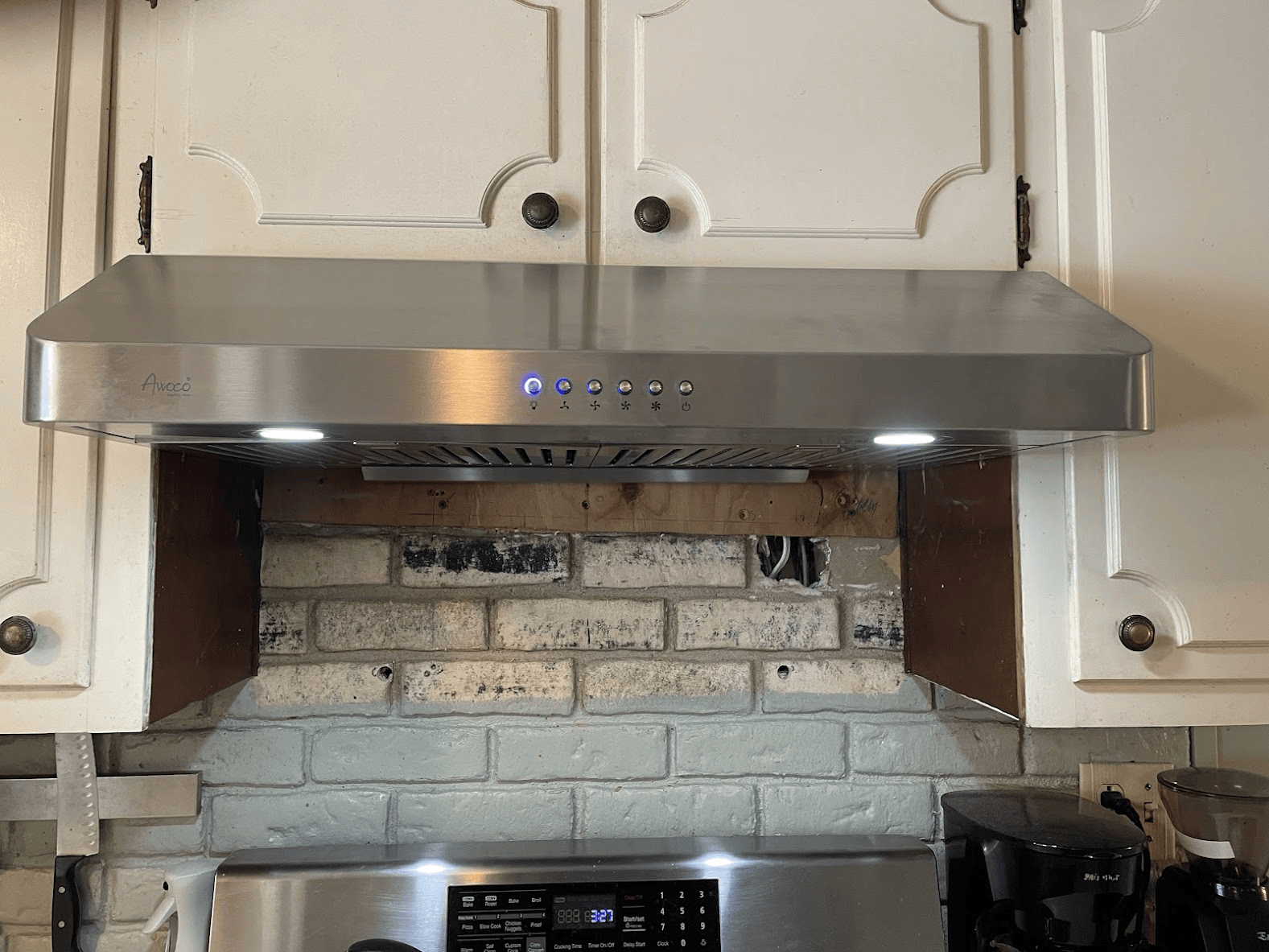 A stainless steel hood is hanging over a brick wall in a kitchen.