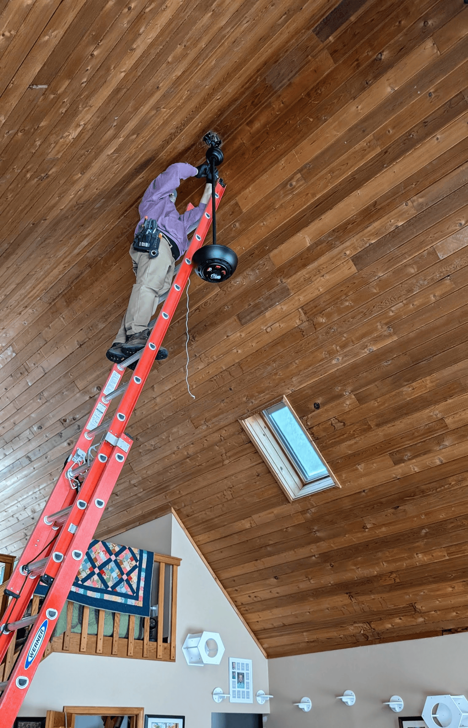 A man is standing on a ladder fixing a light fixture.