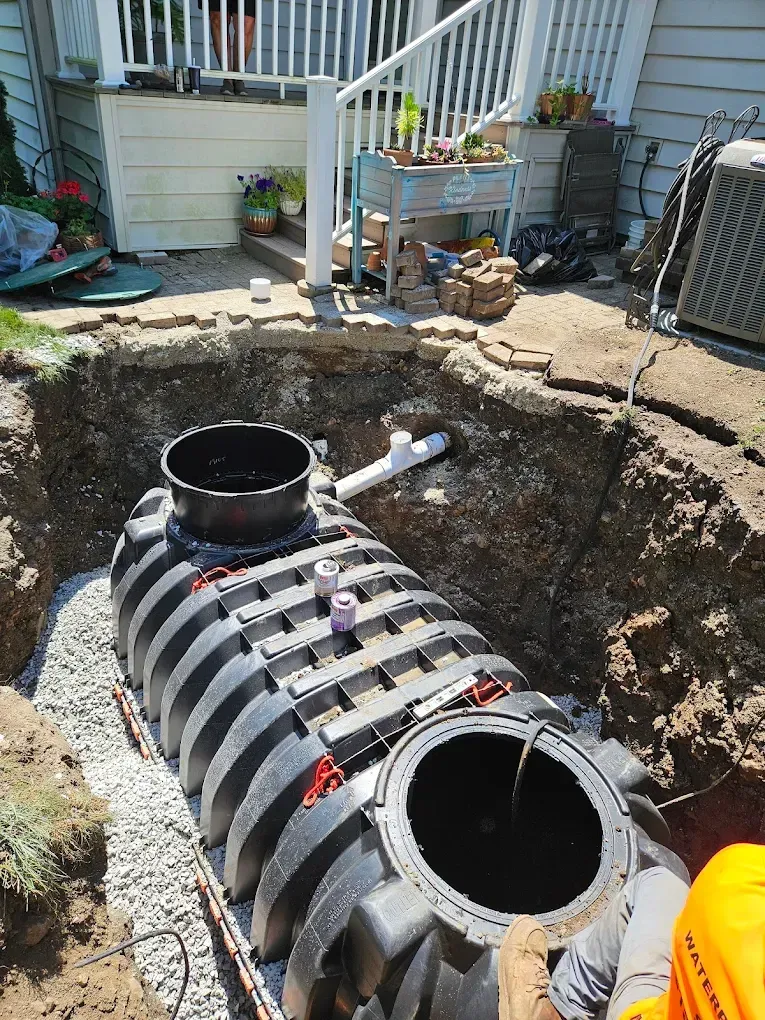 A black plastic septic tank installed in a dug-out hole in the ground near a house.