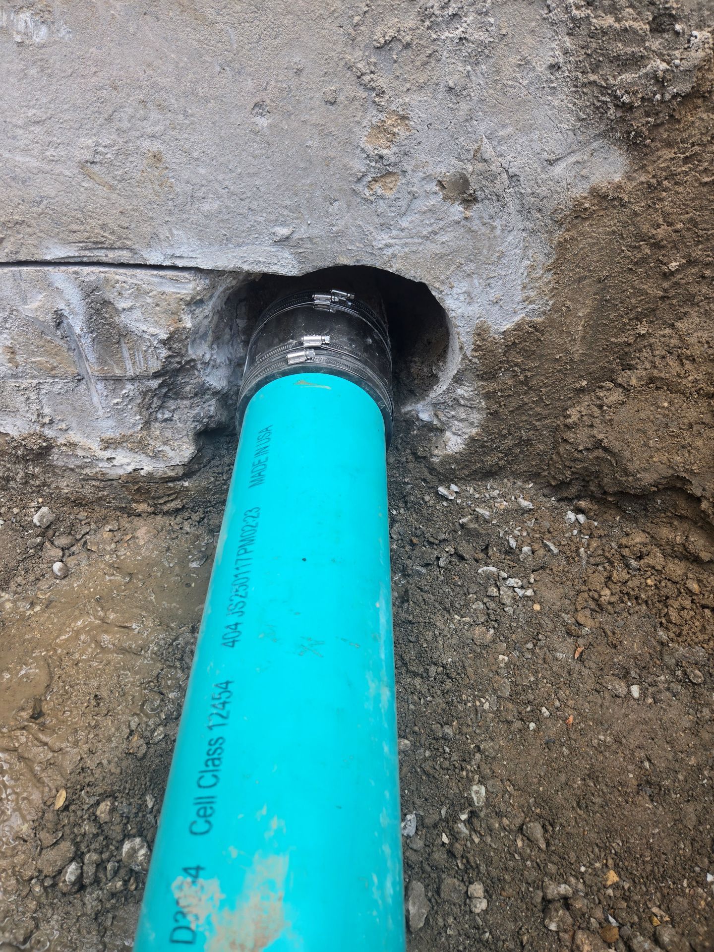 Blue PVC pipe emerging from a hole in a concrete wall, surrounded by soil.