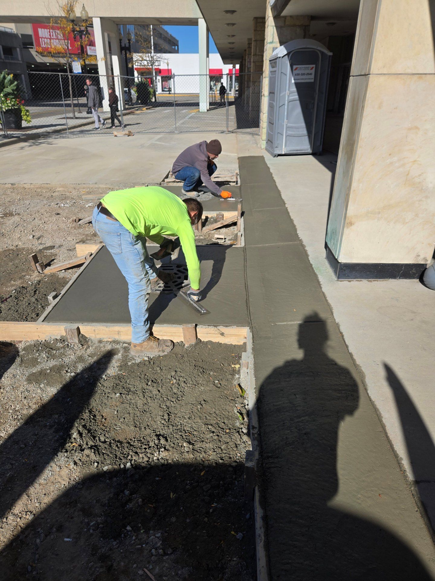 Two workers smoothing fresh concrete sidewalk on a city street.