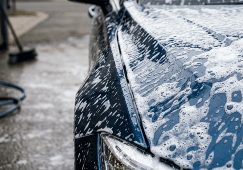 Close-up of a dark blue vehicle covered in soap during a hand car wash