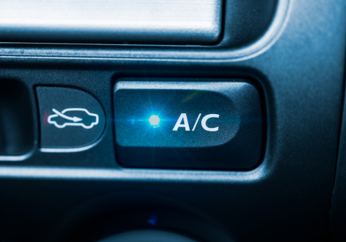Vehicle A/C control button illuminated on a dashboard, representing air conditioning operation