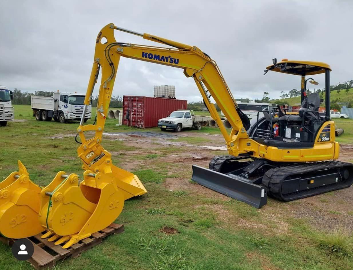 A Yellow Excavator Is Parked In A Grassy Field — Tymmo's Tippers In Yamba, NSW