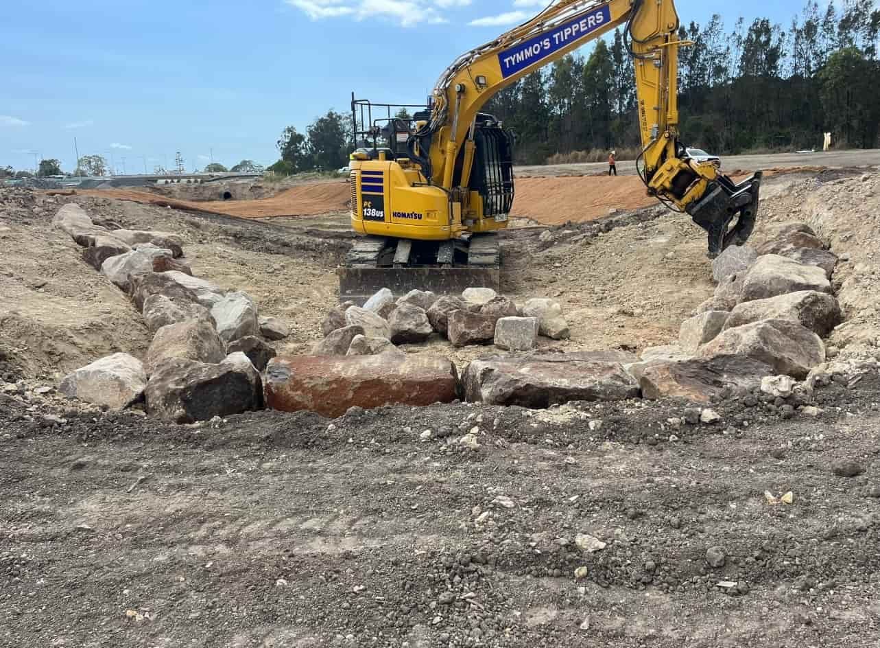 A Yellow Excavator Is Digging A Hole In The Dirt — Tymmo's Tippers In West Ballina, NSW