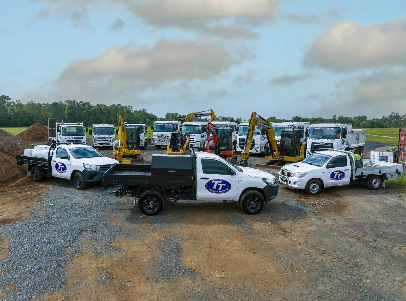 A Group Of Construction Trucks Are Parked In A Gravel Lot — Tymmo's Tippers In West Ballina, NSW