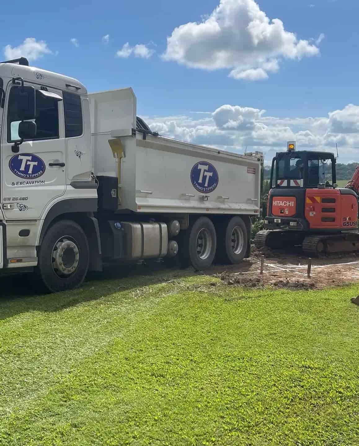 A Dump Truck And An Excavator Are Parked In A Grassy Field — Tymmo's Tippers In Mullumbimby, NSW