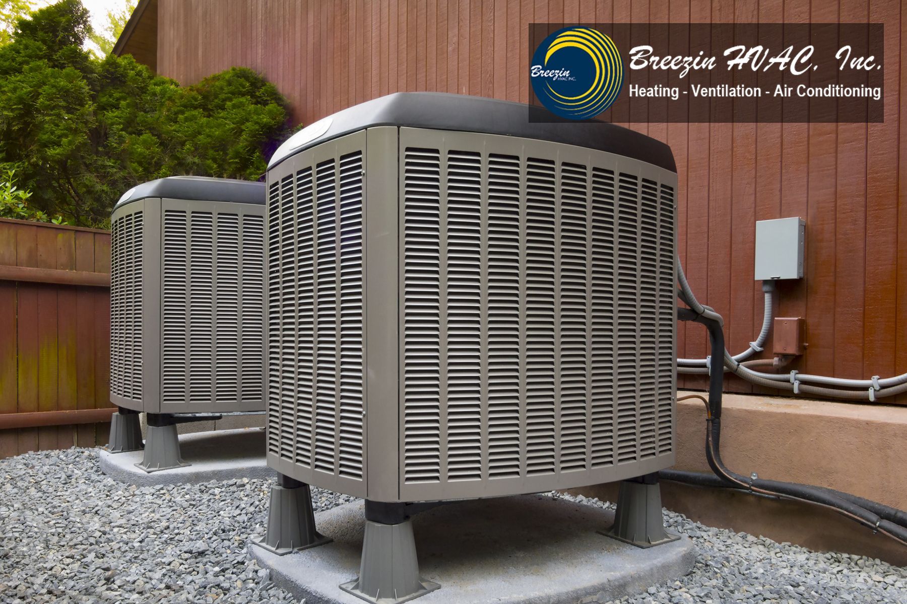 Two outdoor HVAC units on gravel beside a building wall, with pipes and a service label on the unit