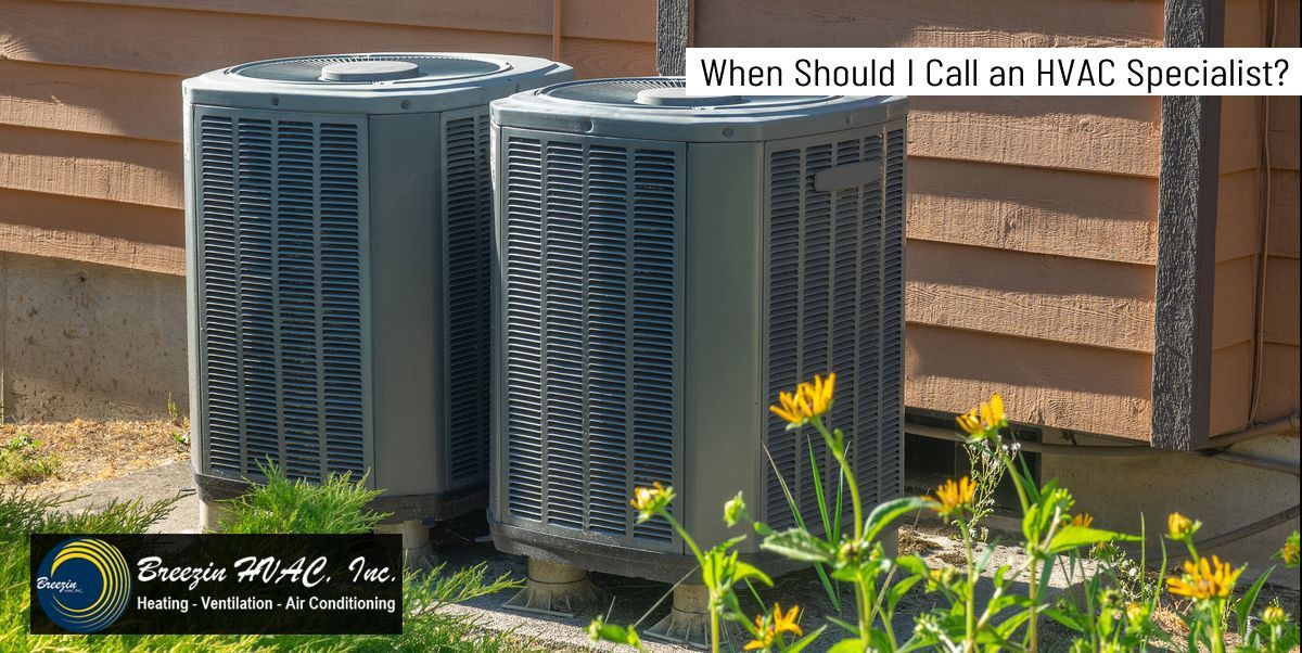 Outdoor HVAC units beside a brick wall with yellow flowers and text: “When Should I Call an HVAC Specialist?”
