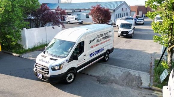 Two white service vans parked in a residential driveway, one near the garage and one on the street.