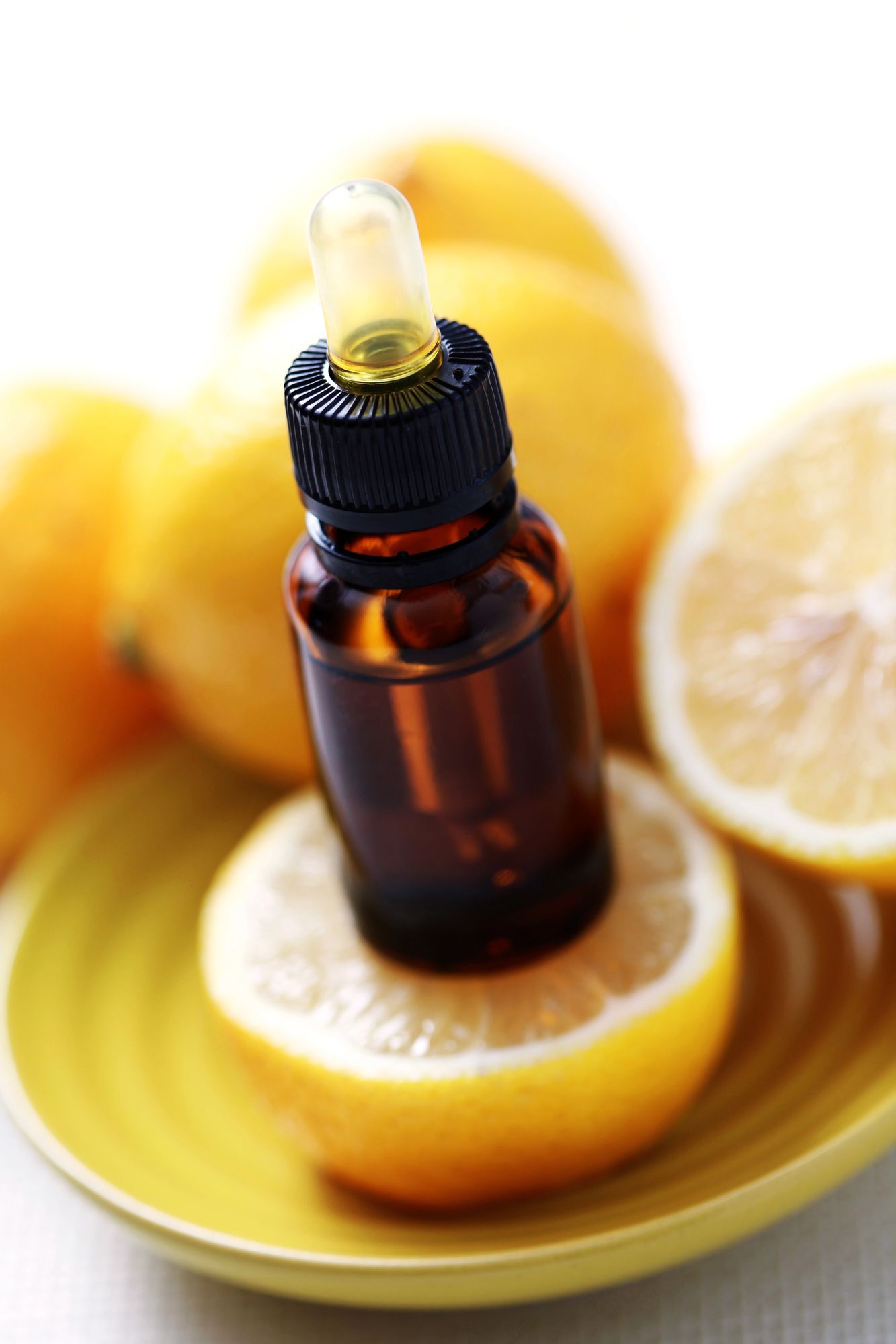 Una bottiglia di olio con contagocce è appoggiata su mezzo limone, circondata da limoni su un piatto giallo.
