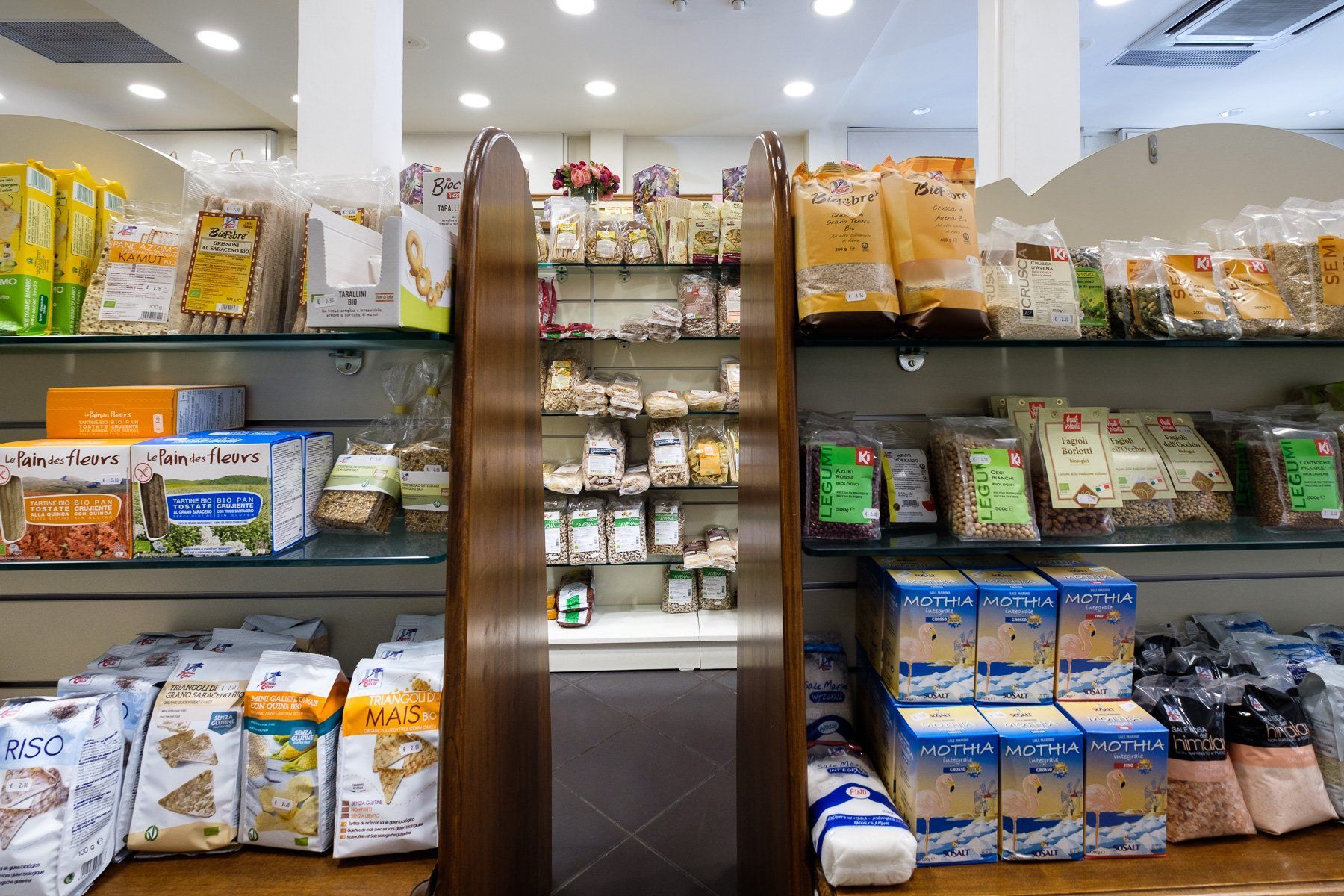Scaffali di un negozio pieni di prodotti alimentari confezionati, supporti in legno.