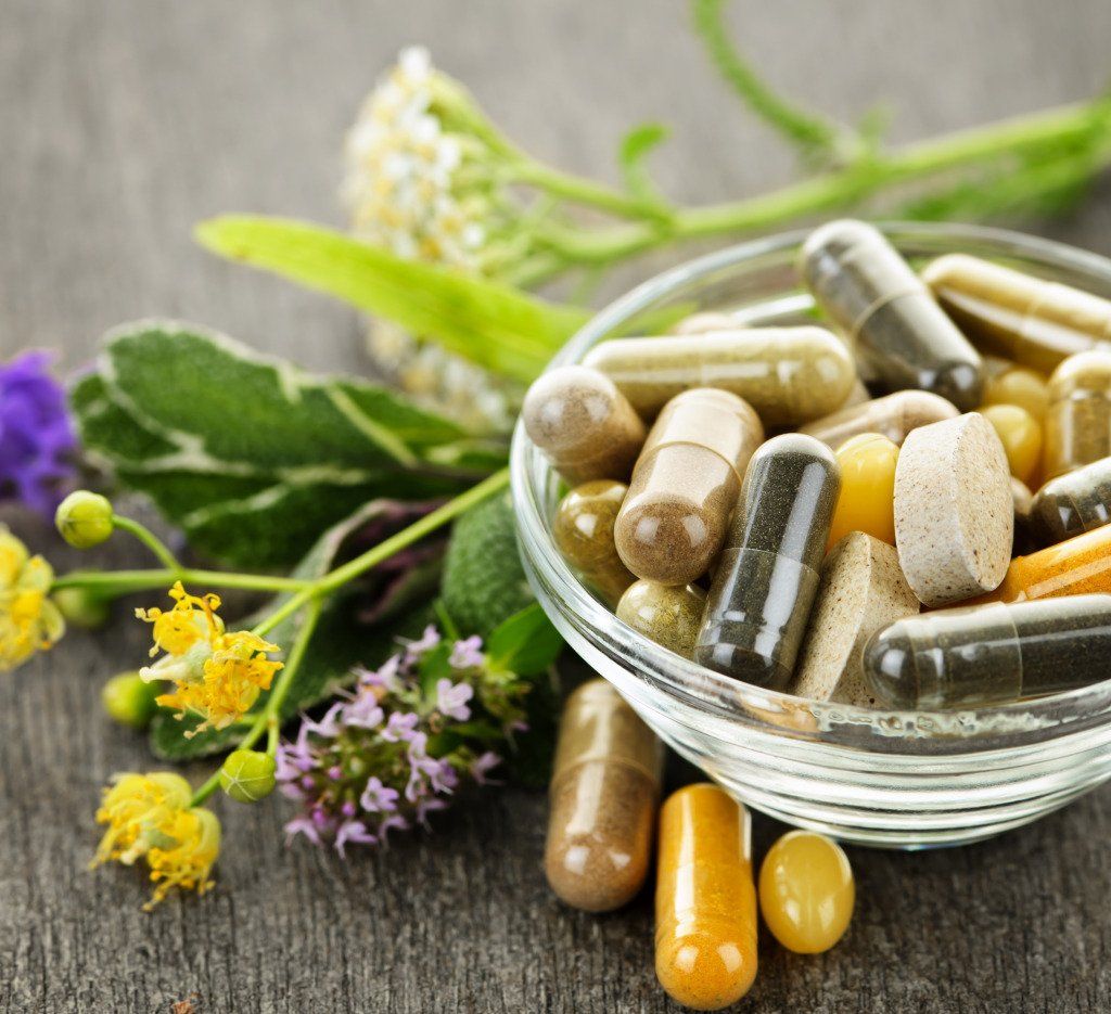 Ciotola con varie pillole e capsule con erbe su una superficie di legno.