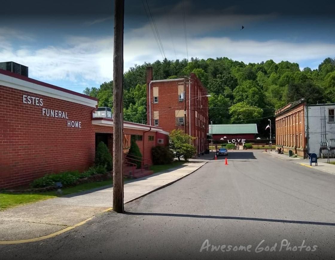 A street view showing the red brick Estes Funeral Home next to an old brick building and a distant white building.