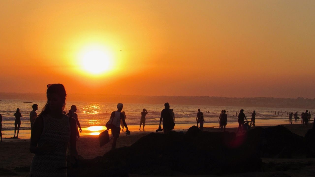 a group of people are walking on a beach at sunset in Albufeira, Portugal.